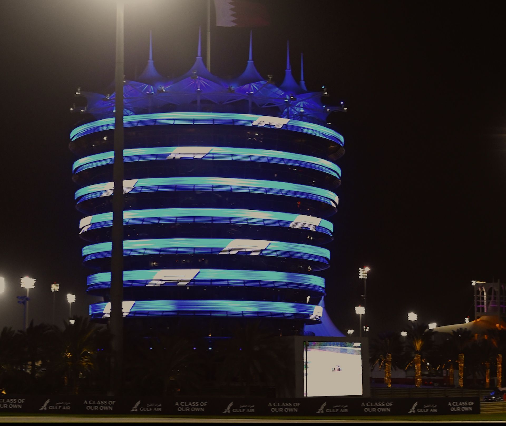 Imagem do guade-reio atrás um telão de led e uma torre circular com leds e no topo bandeira do Bahrain